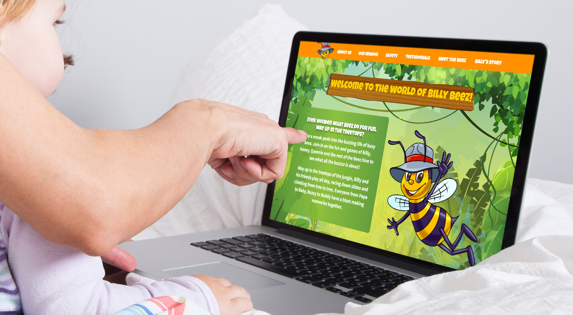 A child and adult sit on a couch while viewing a colorful children's website about Billy Beezi on a laptop. The adult is pointing at the screen, which shows a cartoon bee and welcome text.