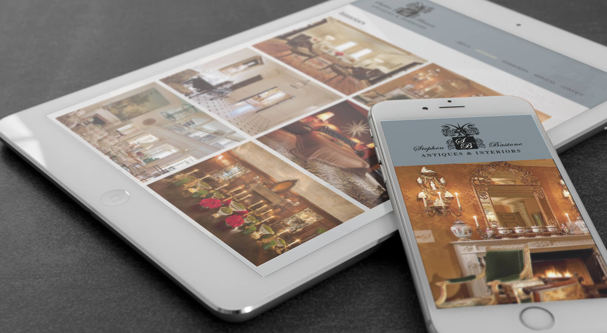 A tablet and smartphone display an antiques and interiors website, showing images of vintage furniture and decor on a dark surface.