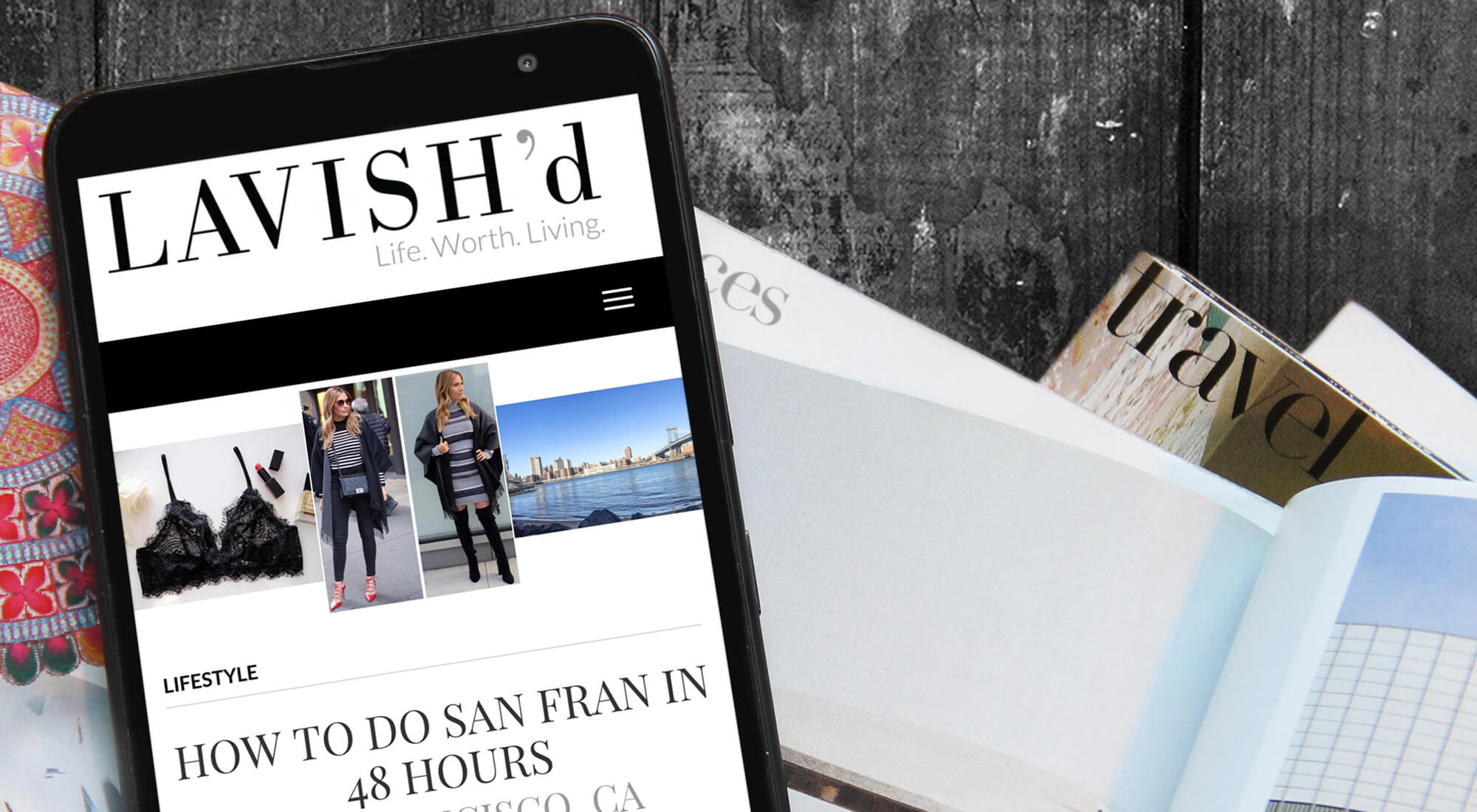 A smartphone displays a lifestyle blog article titled "How to Do San Fran in 48 Hours" next to open magazines on a dark wooden surface.