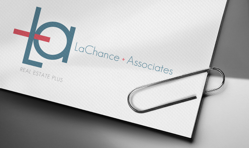A close-up of a paper with the LaChance + Associates Real Estate Plus logo, held by a silver paperclip on a gray surface.