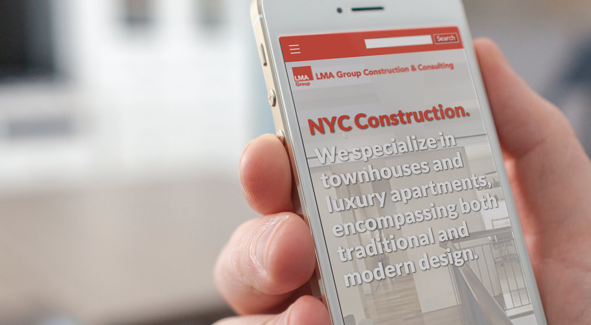 A hand holds a smartphone displaying a website for LMA Group, advertising NYC construction services for townhouses and luxury apartments with traditional and modern design.