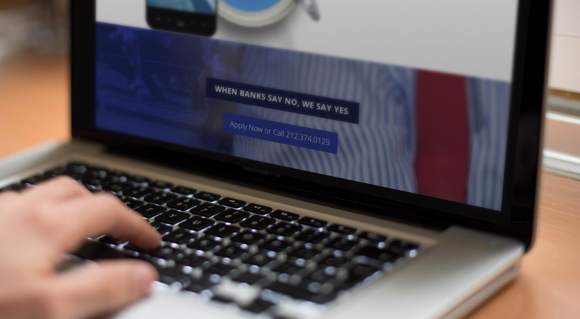 A person using a laptop displaying a webpage with the text "When banks say no, we say yes" and a contact number.