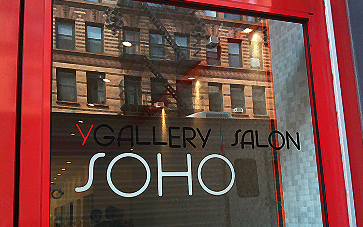 A glass door with the text “YGallery Salon SOHO” in black and red letters, reflecting an apartment building and fire escape across the street.