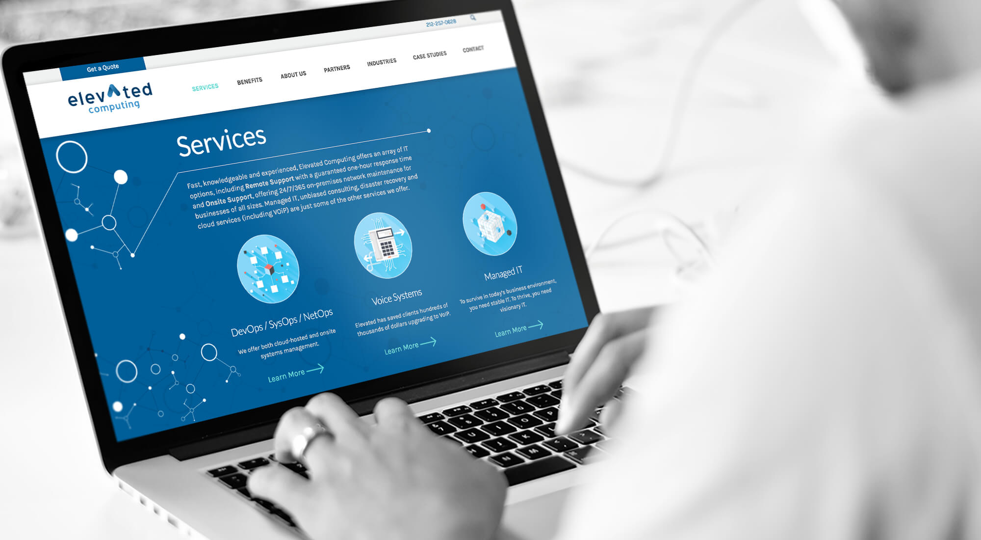 A person types on a laptop displaying the "Services" page of Elevated Computing, featuring descriptions for DevOps, Voice Systems, and Managed IT services.