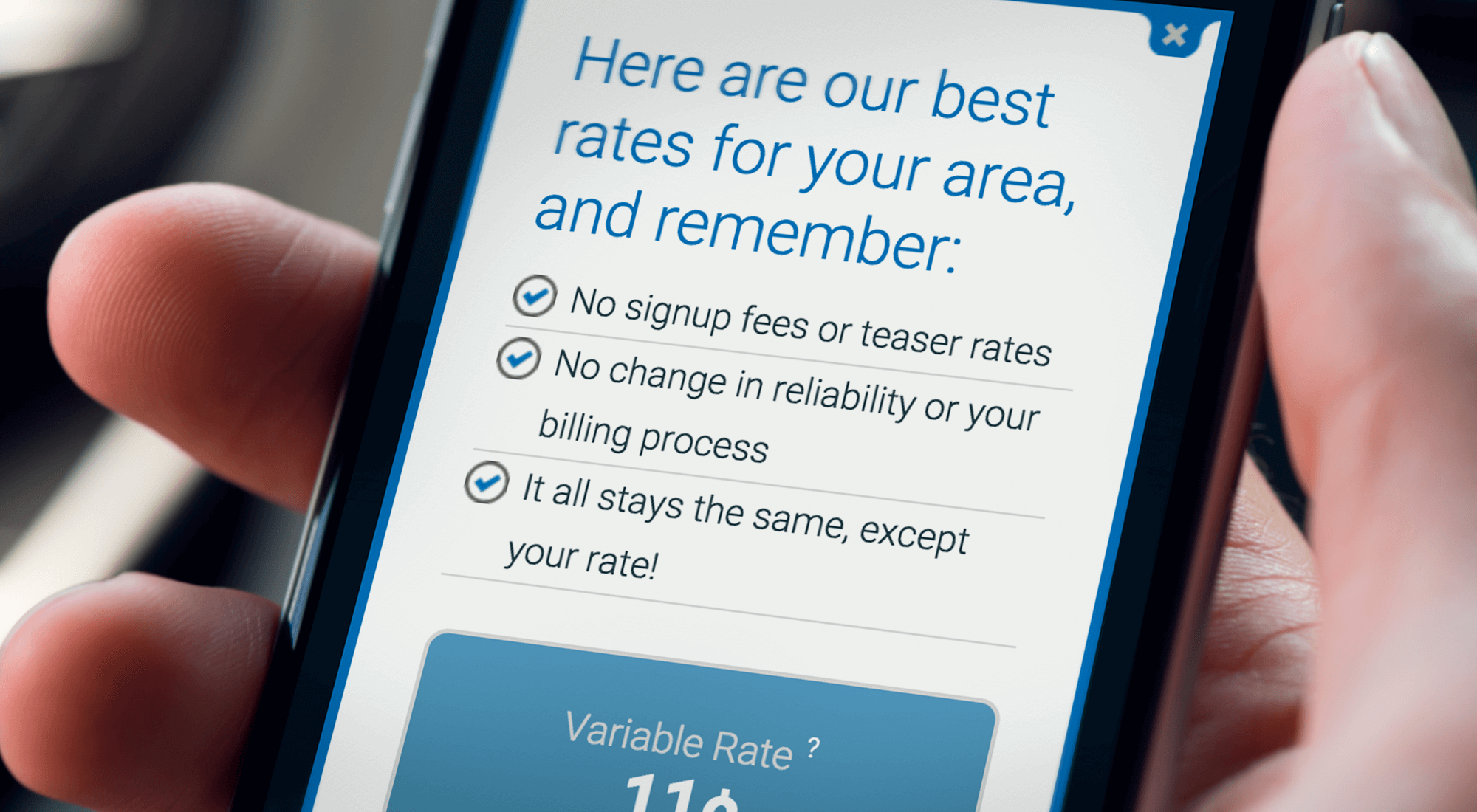 A hand holds a smartphone displaying a webpage listing best rates with three check-marked points about signup, reliability, and consistency in billing.