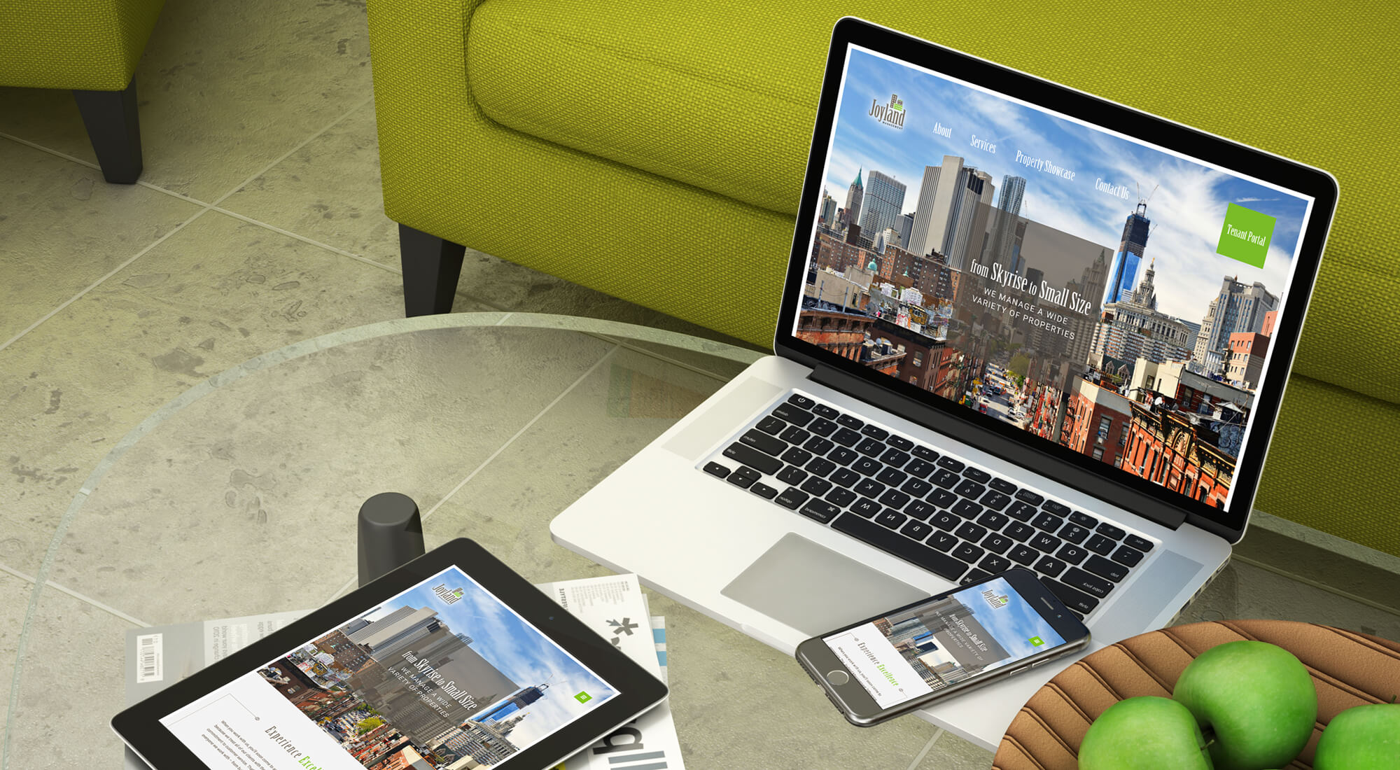 A laptop, tablet, and smartphone displaying the same website are on a glass table beside a bowl of green apples and a green sofa.