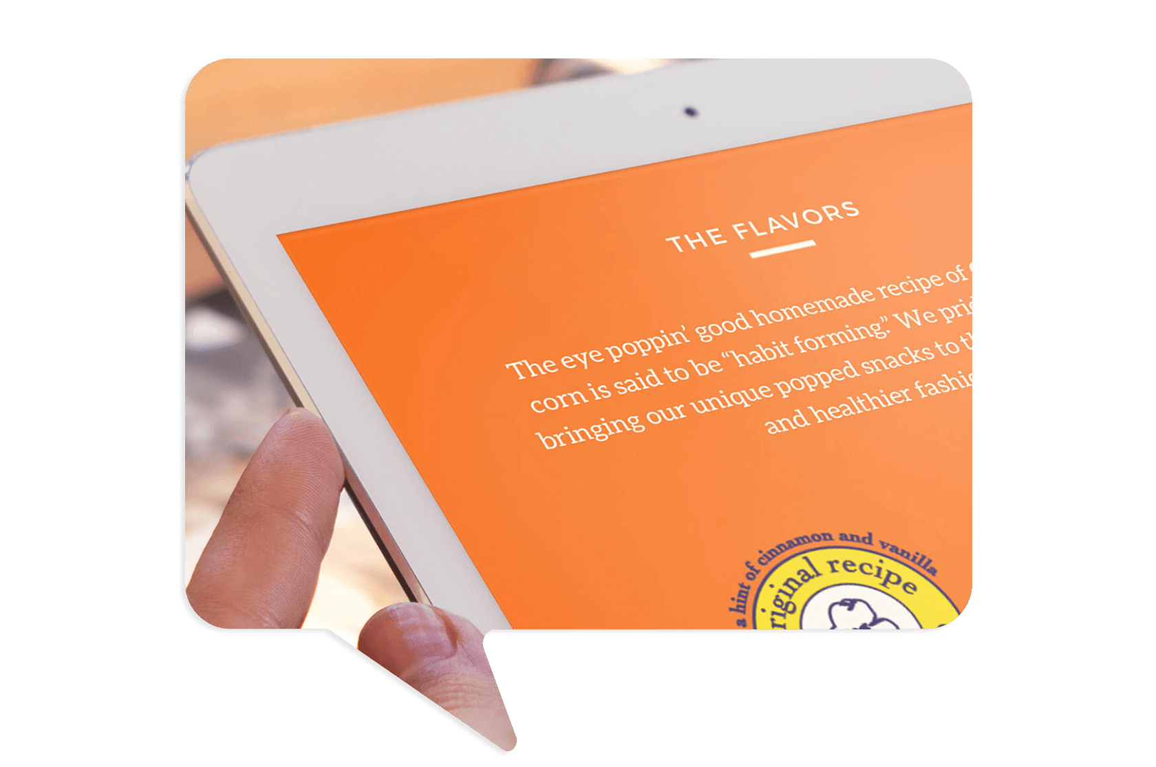 A person holds a tablet displaying a webpage with an orange background, text about popcorn flavors, and a partial view of a circular original recipe label.