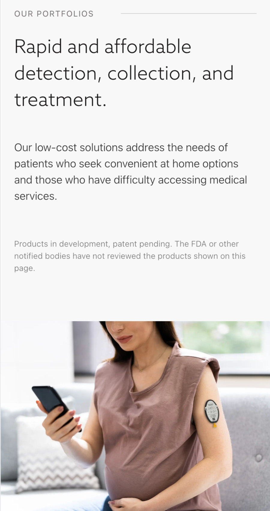 A pregnant woman sits on a couch using a smartphone, with a medical sensor attached to her upper arm—a snapshot of modern healthcare and technology website design in everyday life.