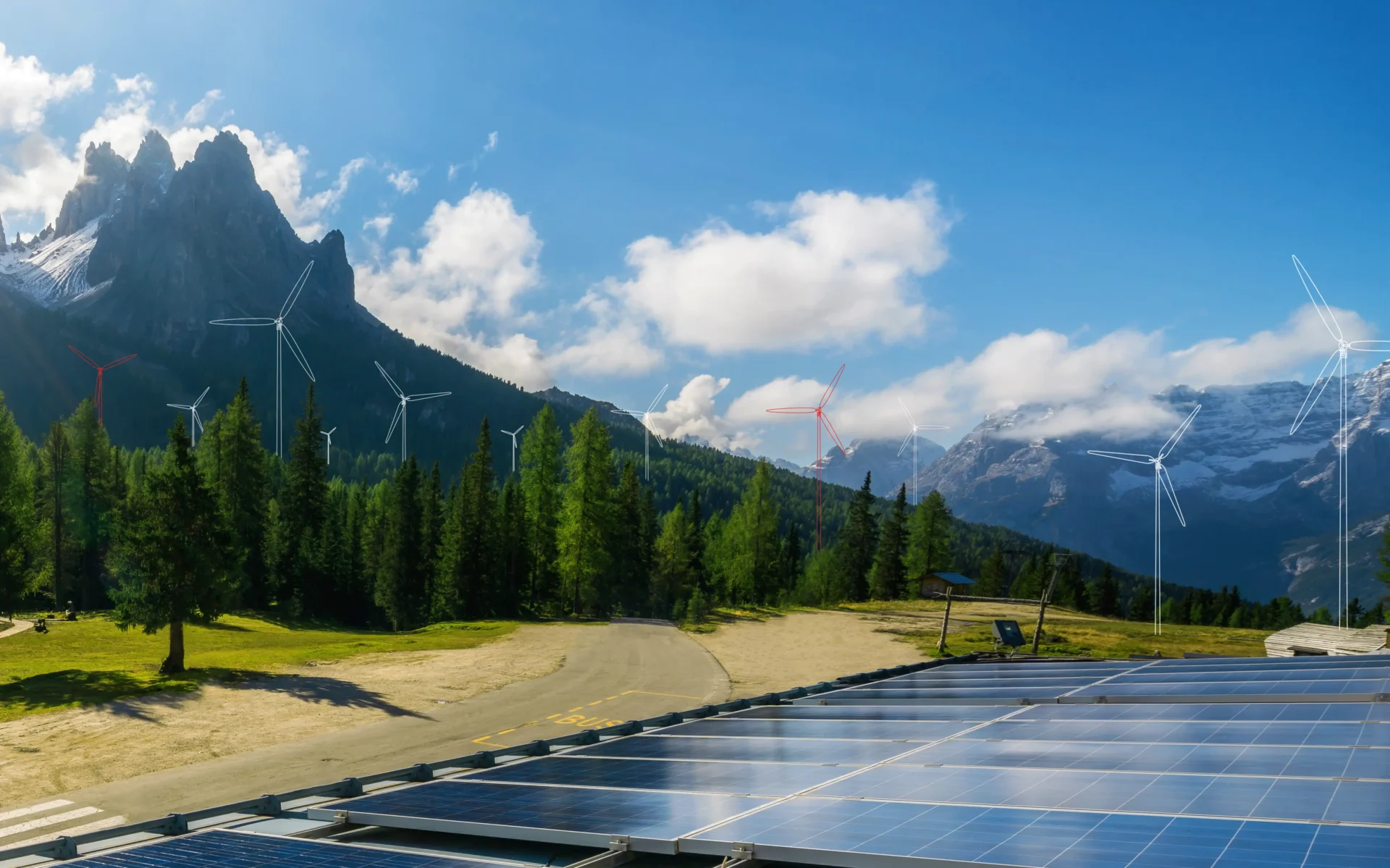 Solar panels in the foreground and wind turbines among trees in a mountain landscape under a blue sky with clouds.