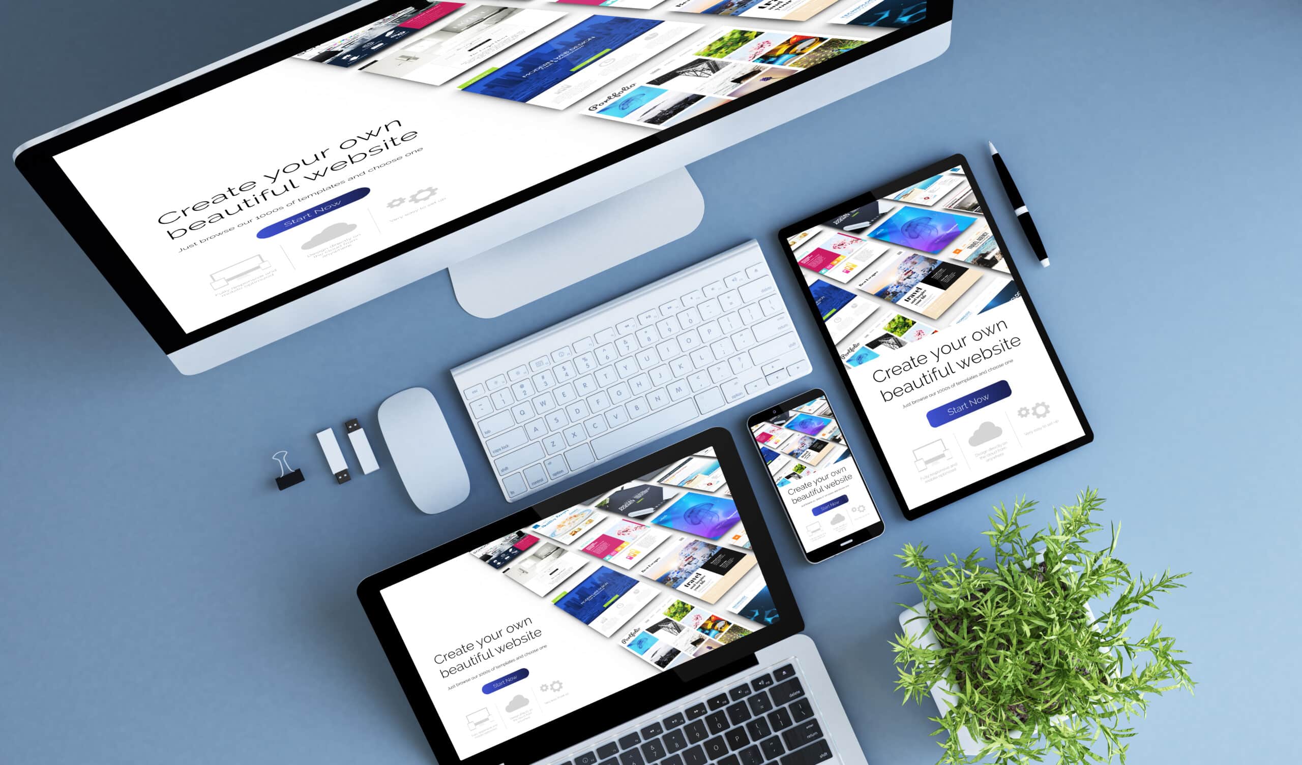 A desktop computer, laptop, tablet, and smartphone on a blue desk display the same website. Accessories and a potted plant are also arranged on the desk.