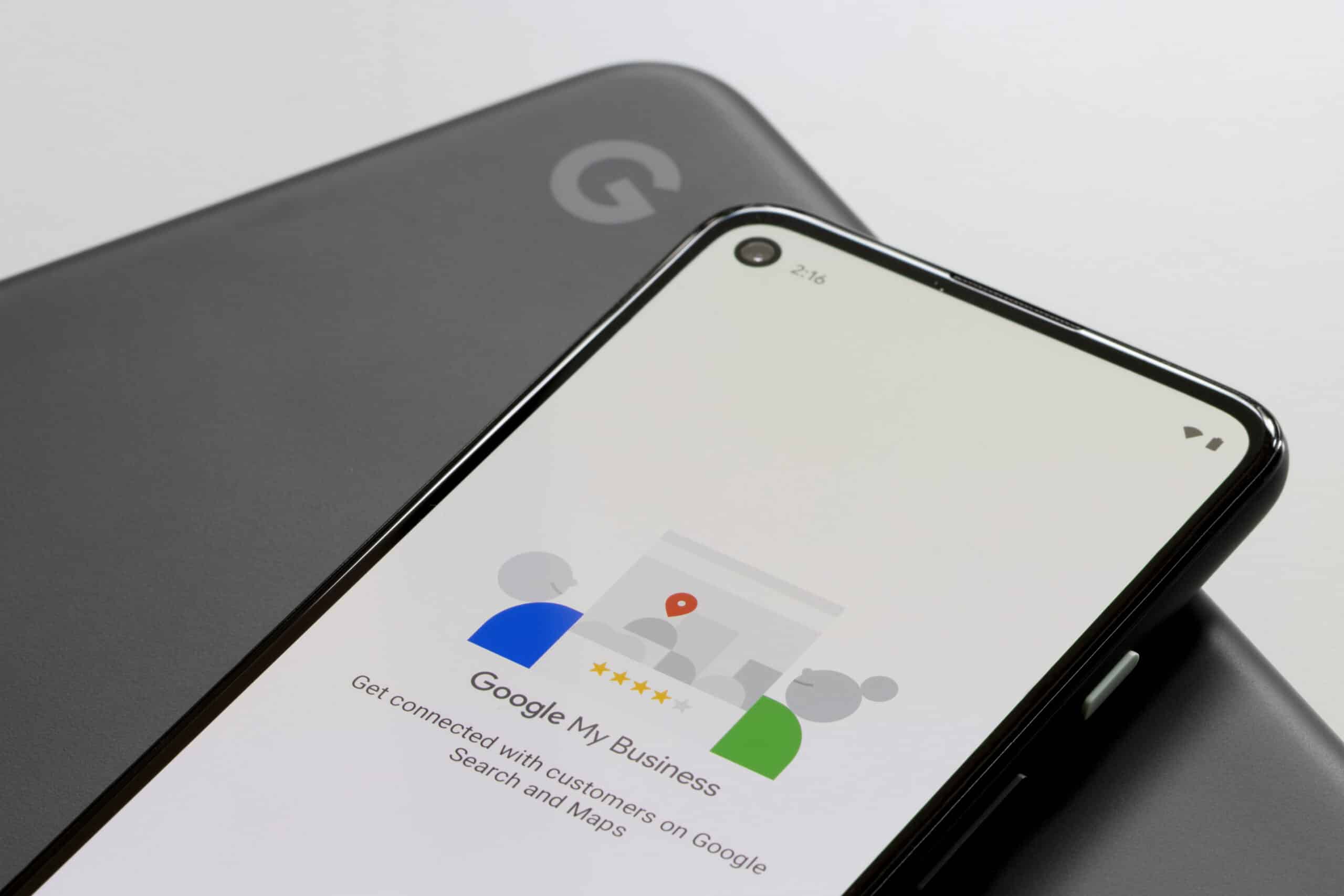 A smartphone displays the Google My Business app welcome screen, resting on a closed, dark gray laptop with a visible Google logo.