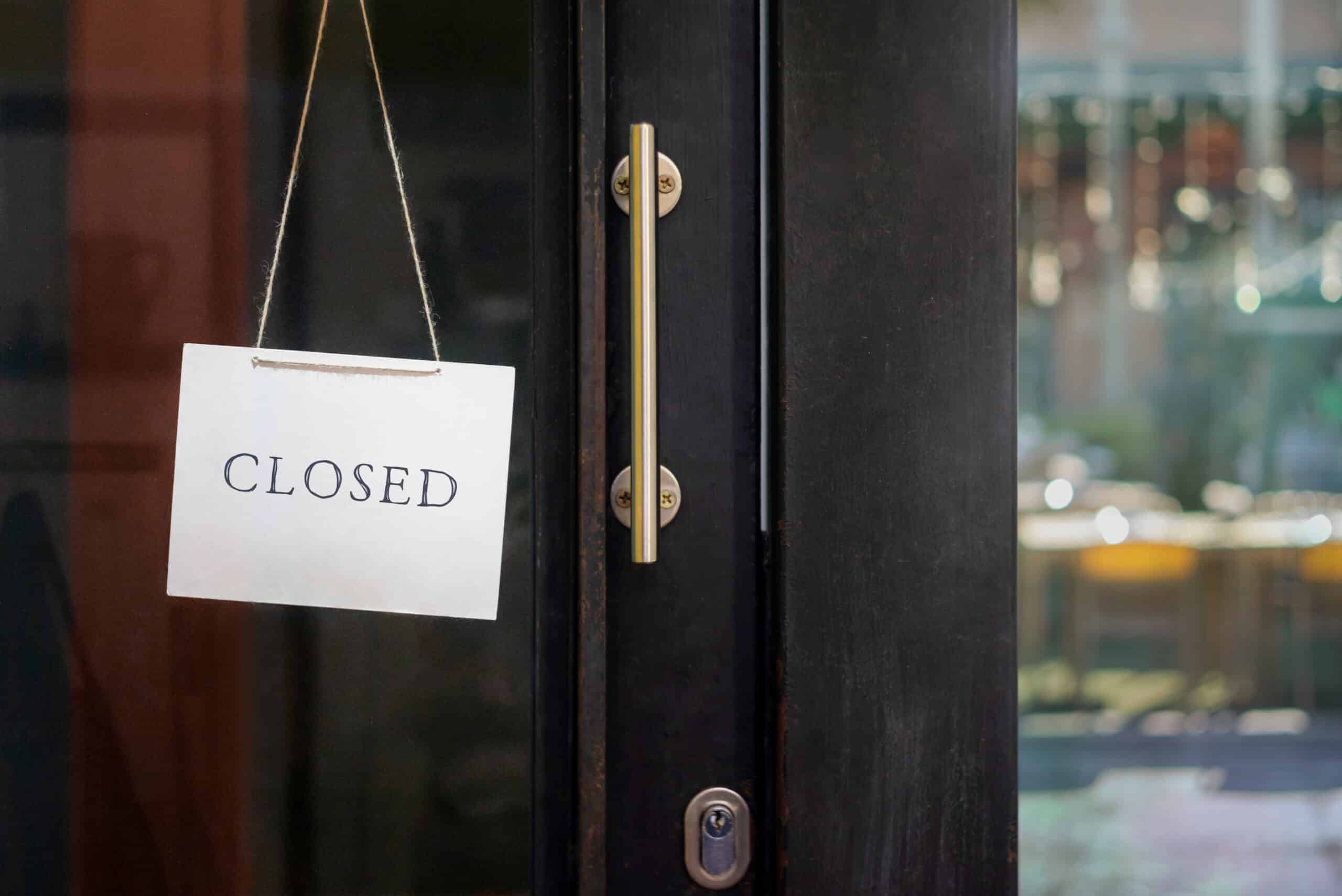 A white sign with the word "CLOSED" hangs on a glass door next to a vertical metal handle, visually echoing the frustration of encountering a website outage.