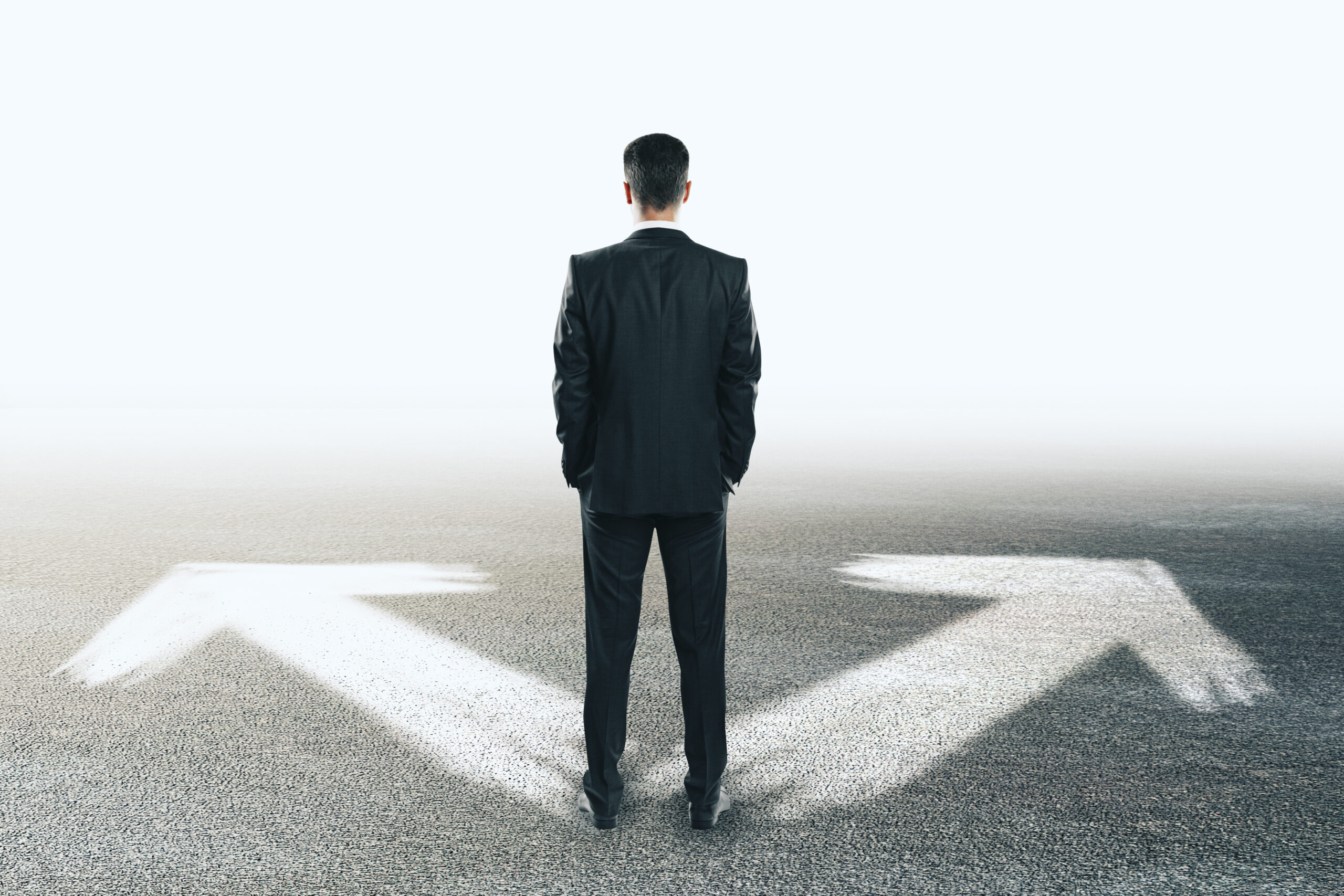A man in a suit stands facing two large white arrows on the ground pointing left and right, symbolizing a choice or decision.